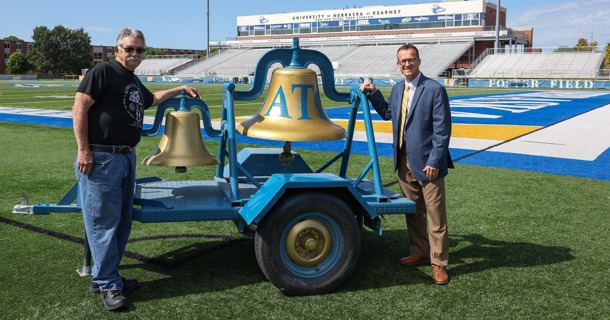 Former Phi Tau Gamma/Alpha Tau Omega fraternity member Tom Paxson, left, and UNK Athletic Director Marc Bauer are pictured with the Loper Victory Bell at Cope Stadium. (Photo by Erika Pritchard, UNK Communications)